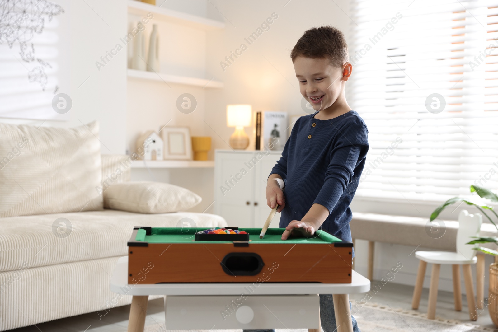 Photo of Cute little boy playing billiards at home