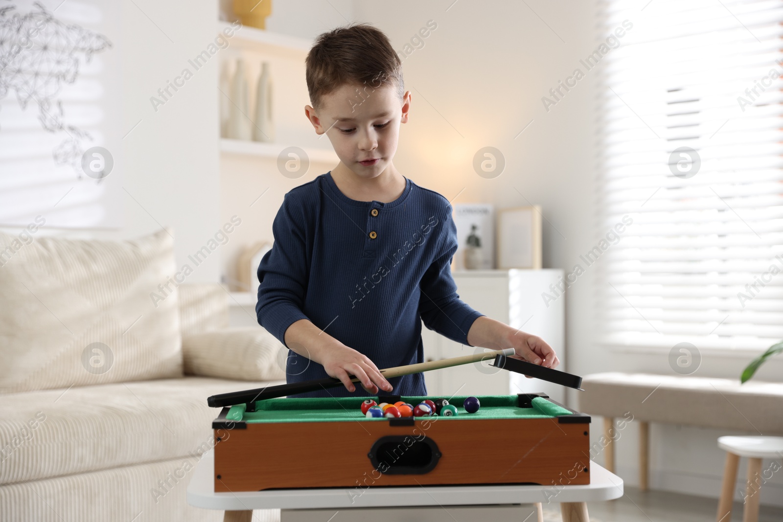 Photo of Cute little boy playing billiards at home