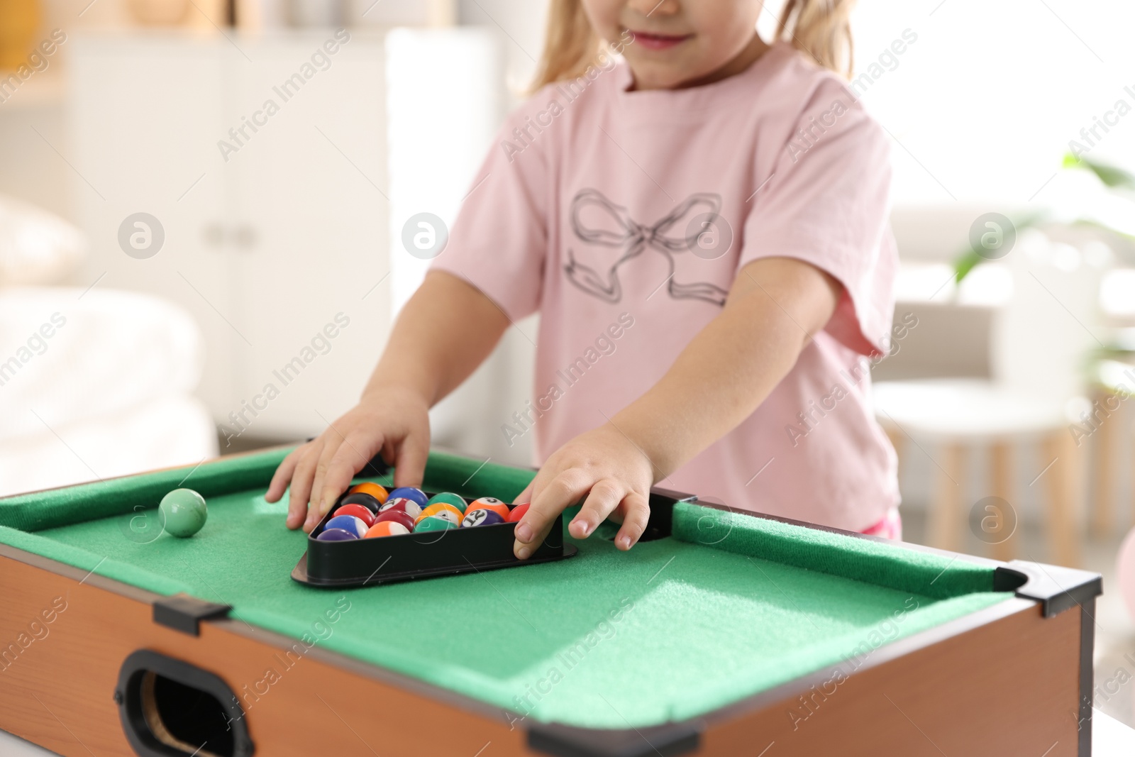 Photo of Little girl with colorful billiard balls in triangle rack at green table, closeup