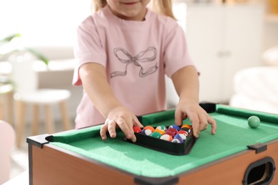 Photo of Little girl with colorful billiard balls in triangle rack at green table, closeup