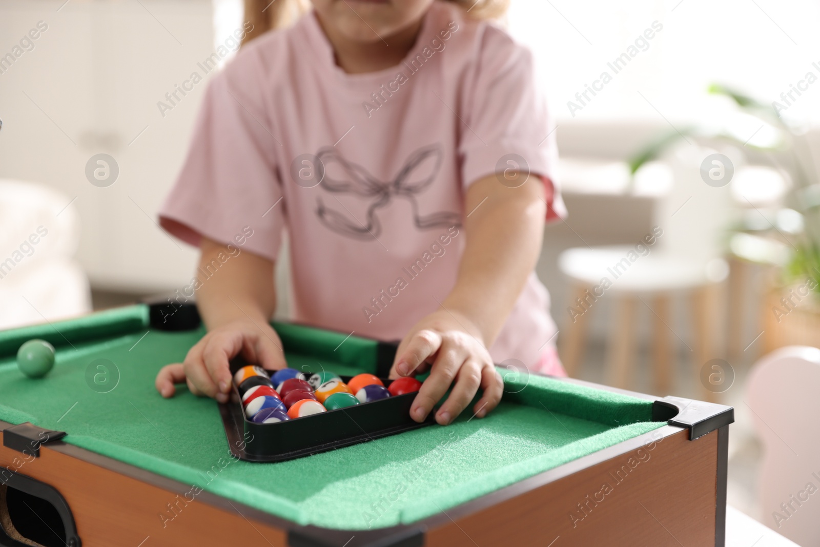 Photo of Little girl with colorful billiard balls in triangle rack at green table, closeup