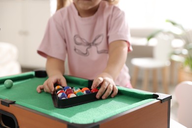 Little girl with colorful billiard balls in triangle rack at green table, closeup