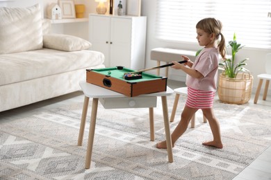 Photo of Cute little girl playing billiards at home