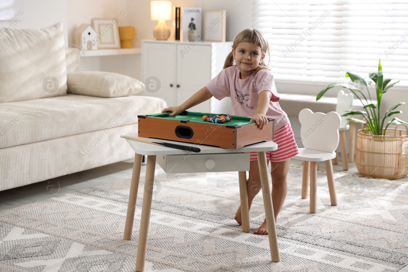 Photo of Cute little girl playing billiards at home