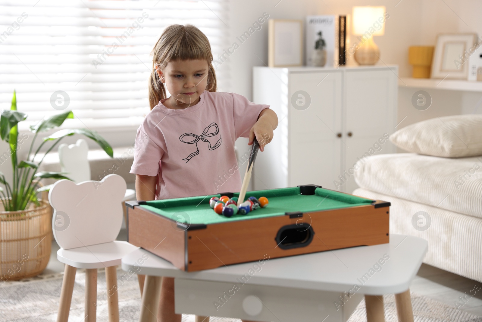 Photo of Cute little girl playing billiards at home