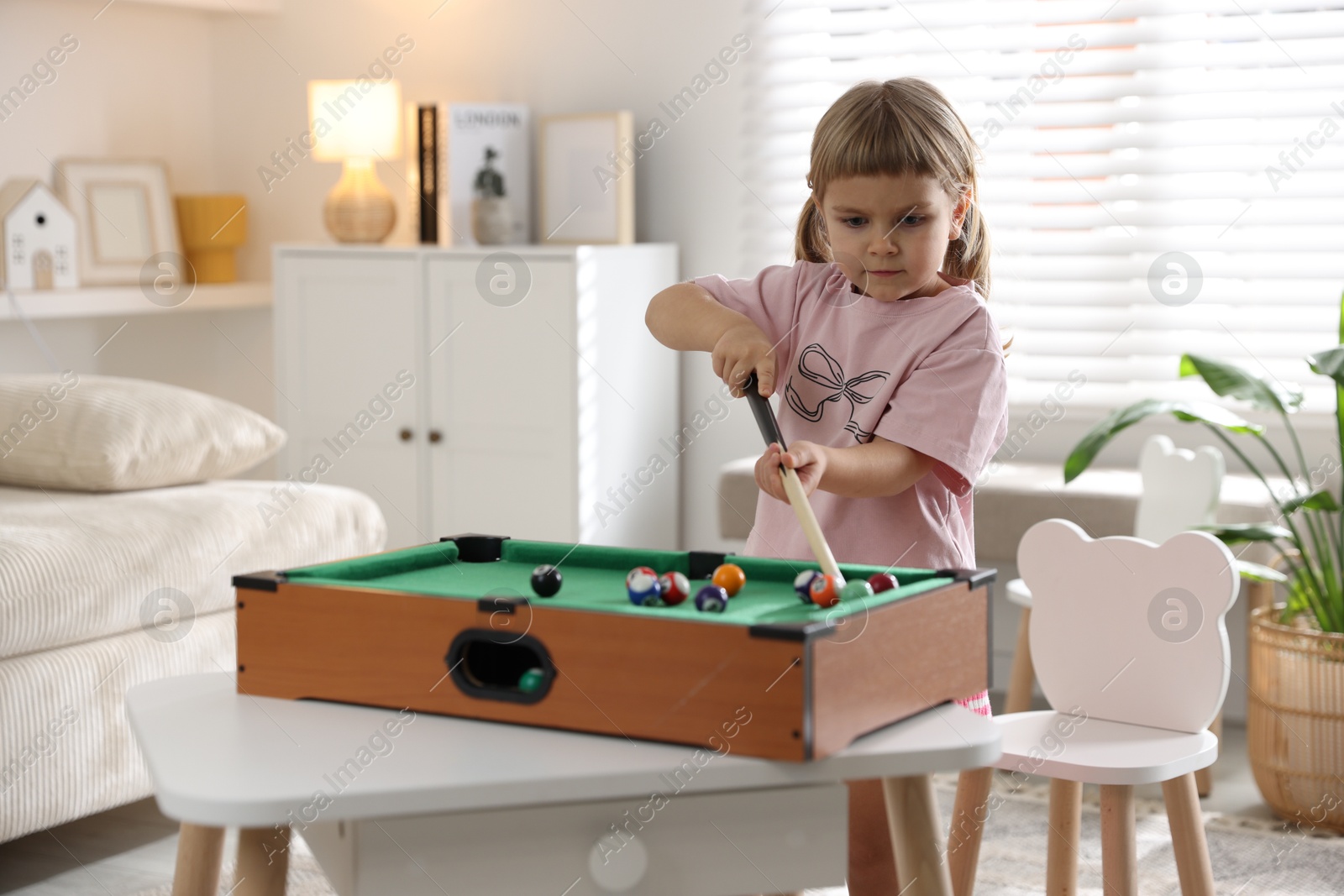 Photo of Cute little girl playing billiards at home