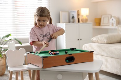 Photo of Cute little girl playing billiards at home