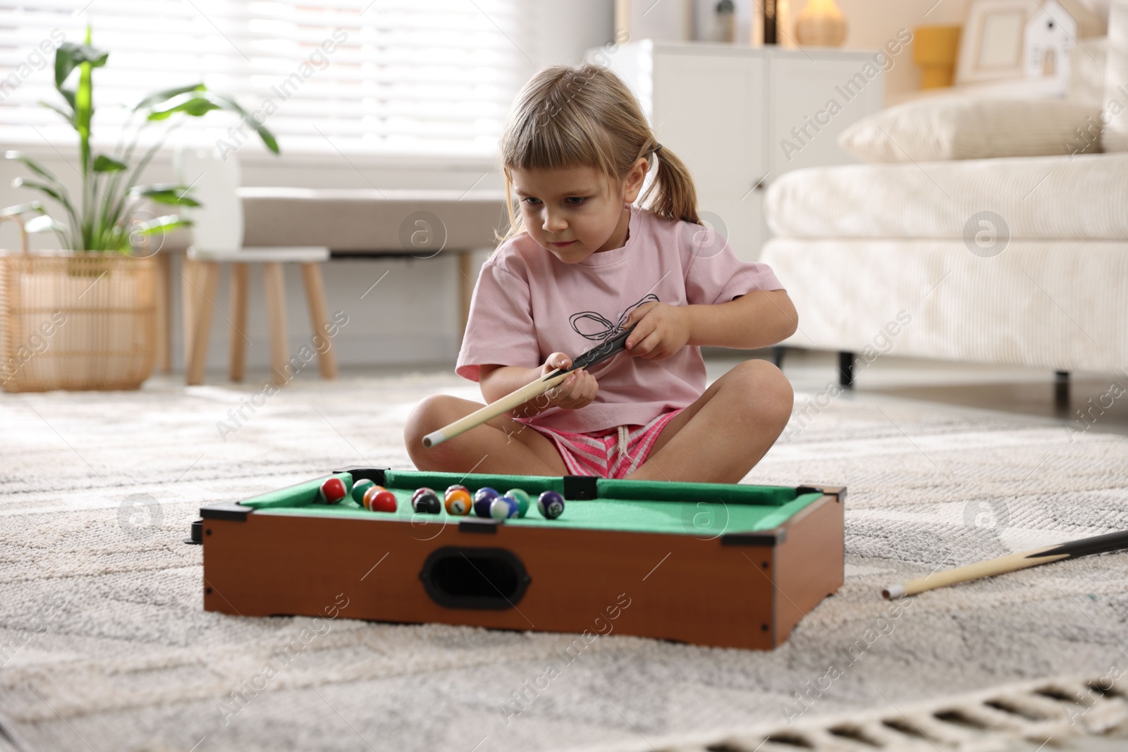 Photo of Cute little girl playing billiards at home