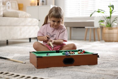 Photo of Cute little girl playing billiards at home