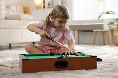 Photo of Cute little girl playing billiards at home