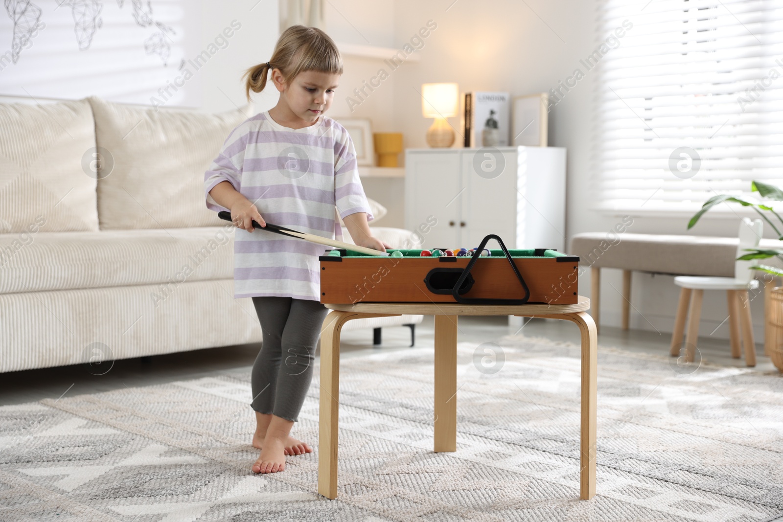 Photo of Cute little girl playing billiards at home