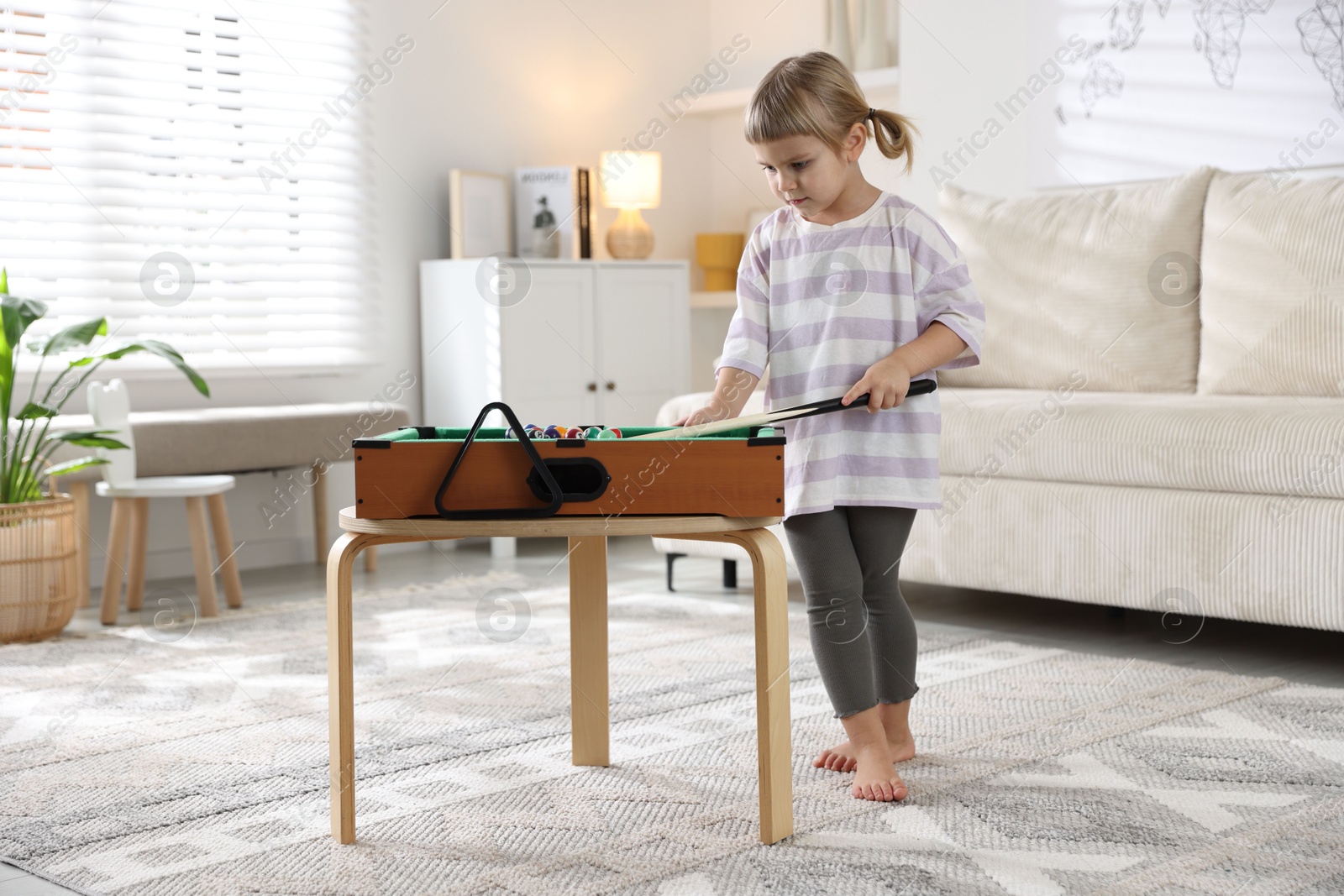 Photo of Cute little girl playing billiards at home