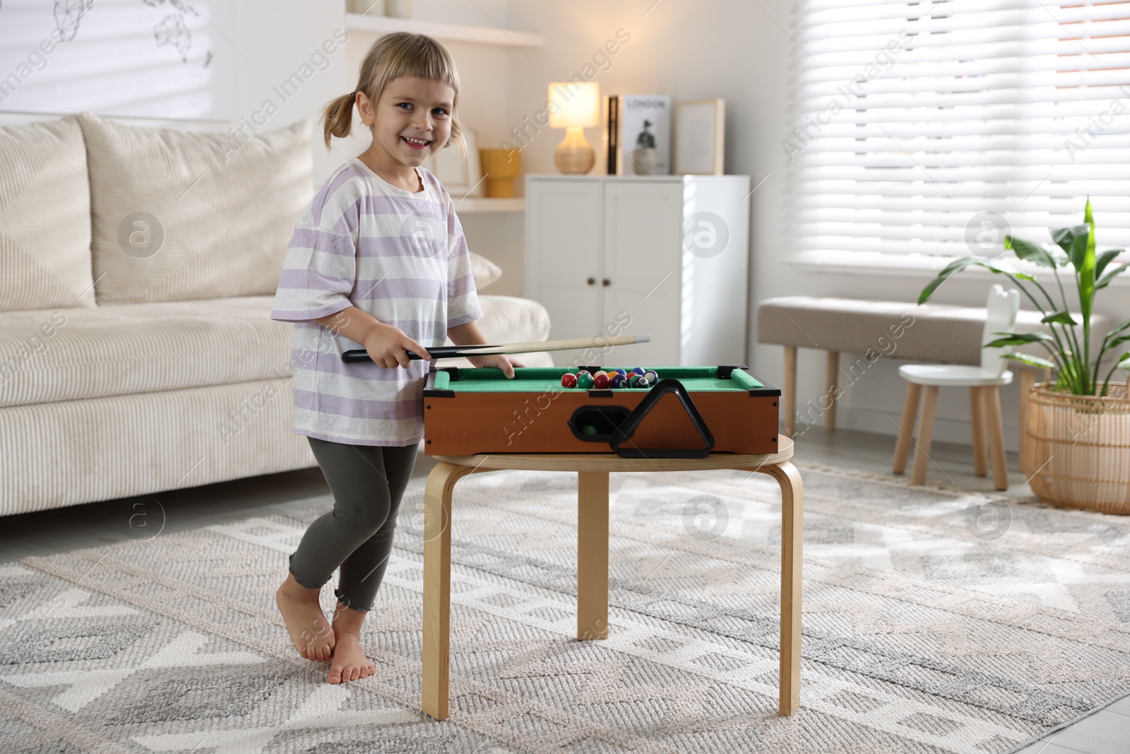 Photo of Cute little girl playing billiards at home