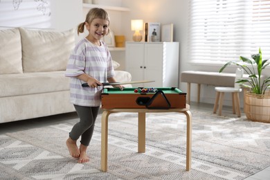 Photo of Cute little girl playing billiards at home