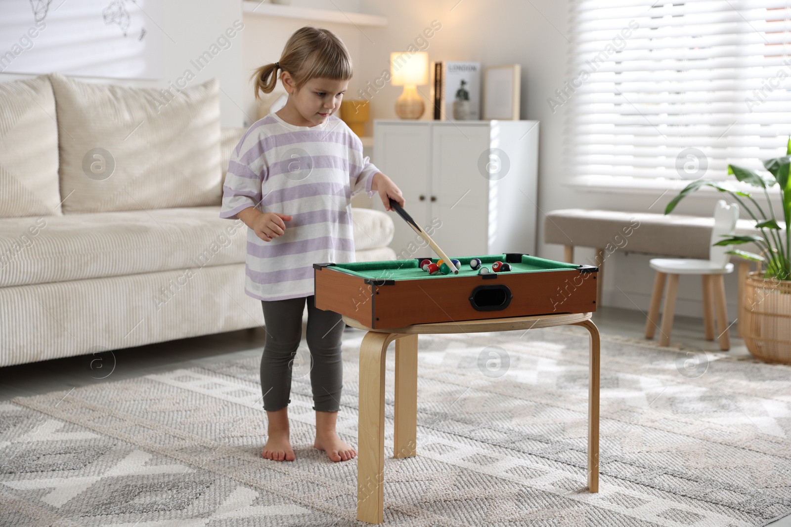 Photo of Cute little girl playing billiards at home