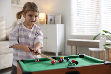 Photo of Cute little girl playing billiards at home