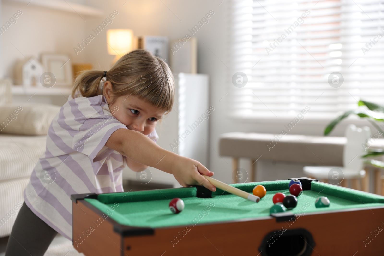 Photo of Cute little girl playing billiards at home