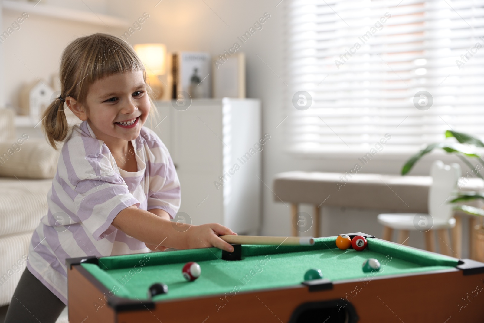 Photo of Cute little girl playing billiards at home