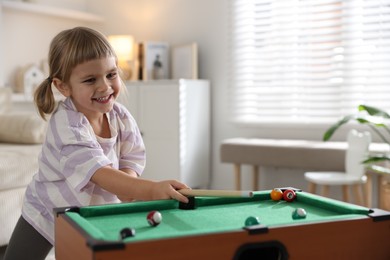 Photo of Cute little girl playing billiards at home