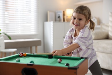 Photo of Cute little girl playing billiards at home