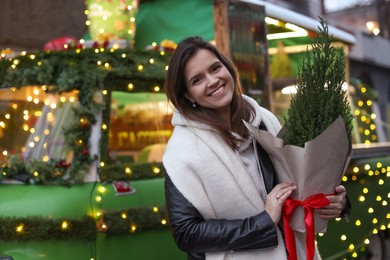 Photo of Happy woman with thuja tree near Christmas bus outdoors. Space for text