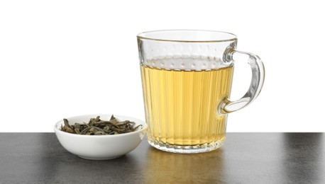 Photo of Refreshing green tea in cup and dry leaves on grey textured table against white background