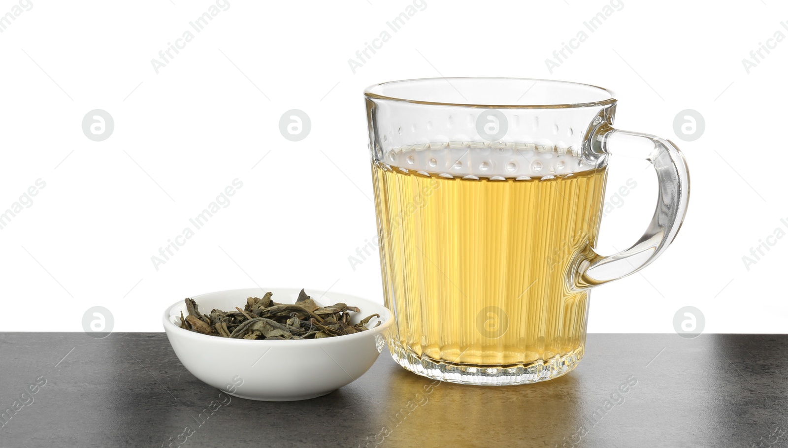 Photo of Refreshing green tea in cup and dry leaves on grey textured table against white background. Space for text