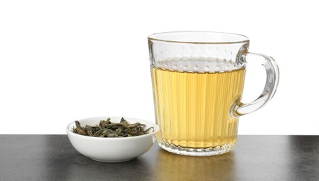 Photo of Refreshing green tea in cup and dry leaves on grey textured table against white background. Space for text