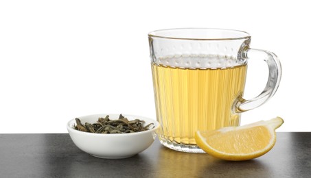 Photo of Refreshing green tea in cup, slice of lemon and dry leaves on grey textured table against white background. Space for text