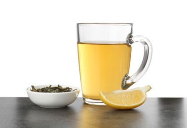 Photo of Refreshing green tea in cup, slice of lemon and dry leaves on grey textured table against white background. Space for text