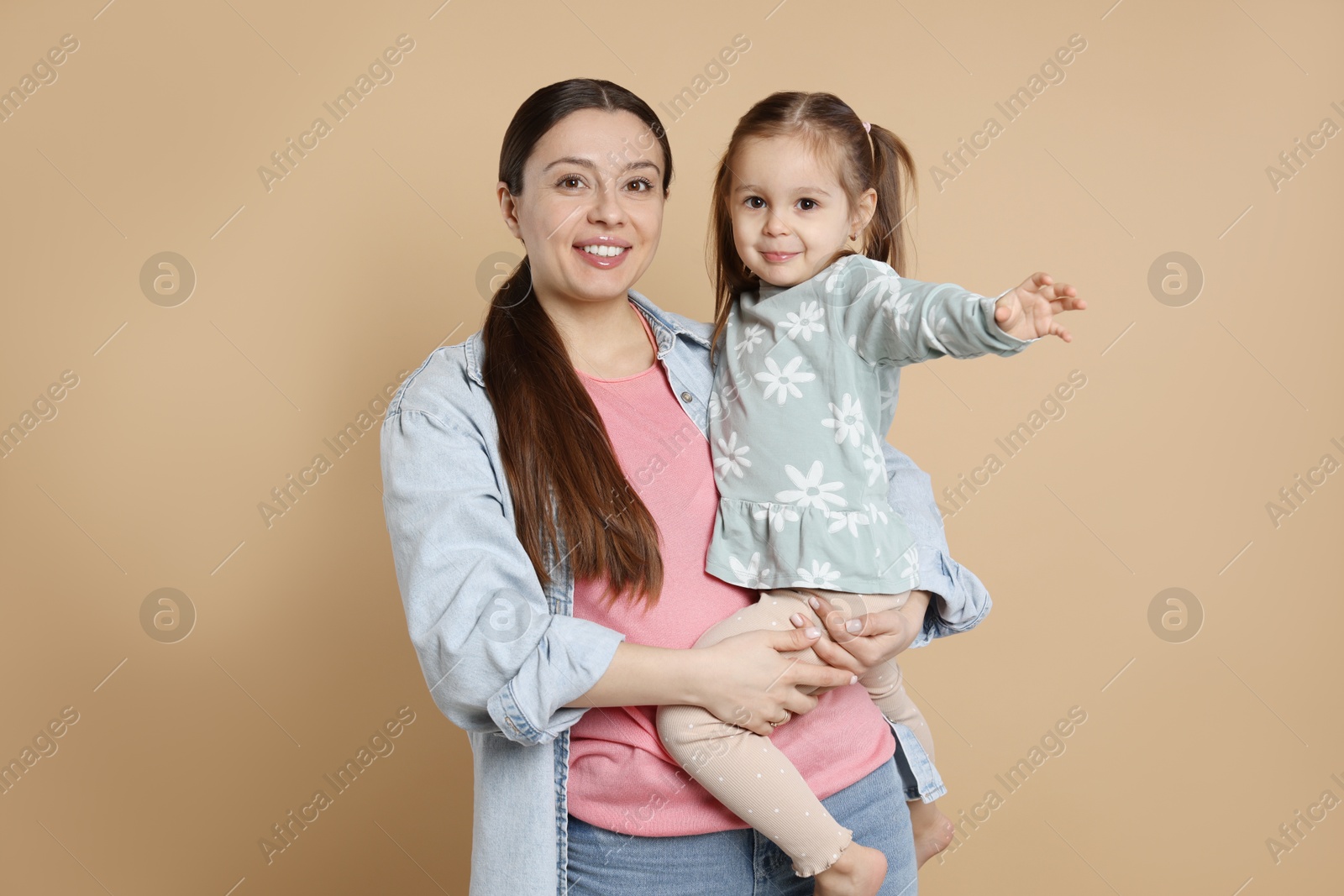 Photo of Portrait of happy mother and her cute little daughter on beige background