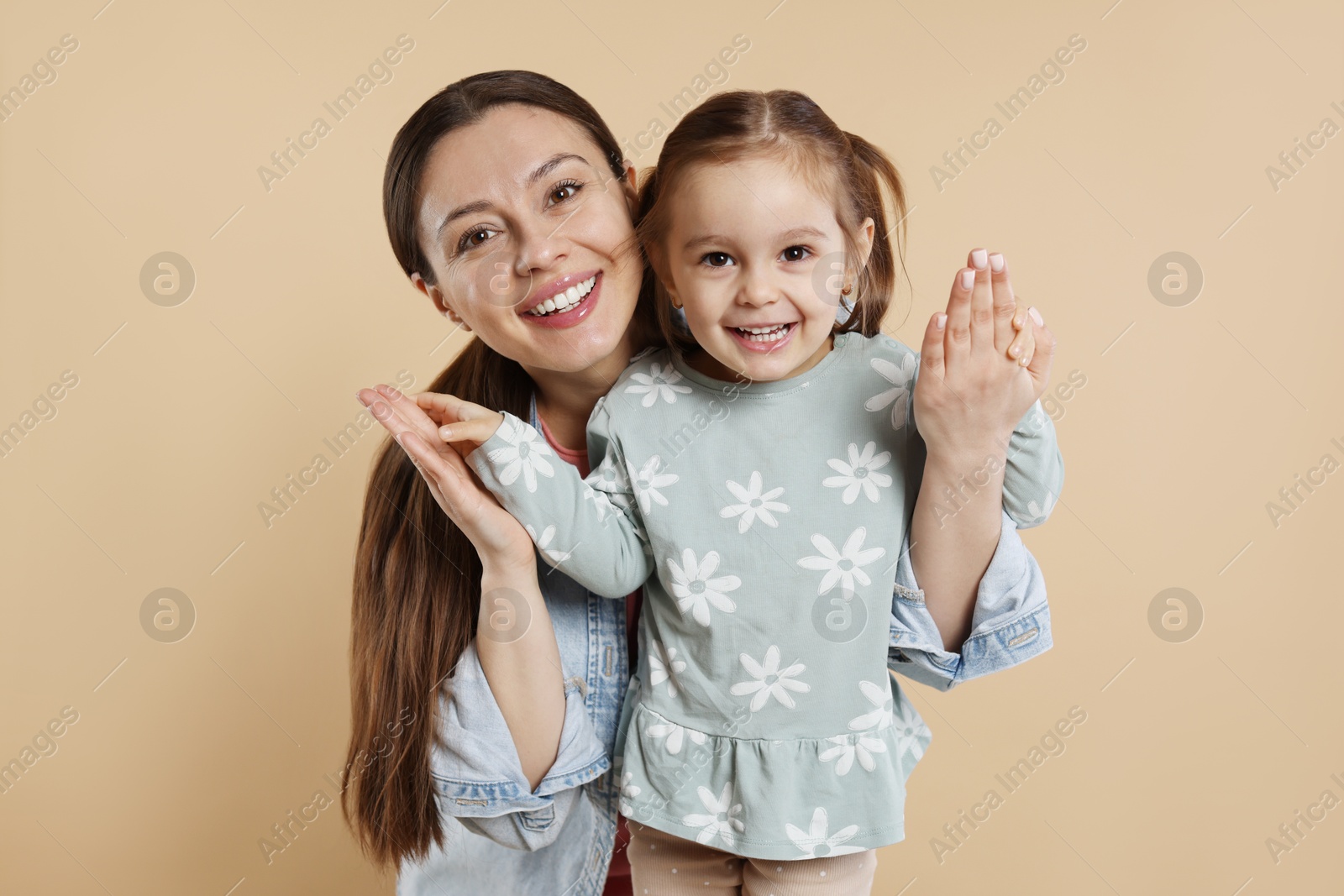 Photo of Portrait of happy mother and her cute little daughter on beige background