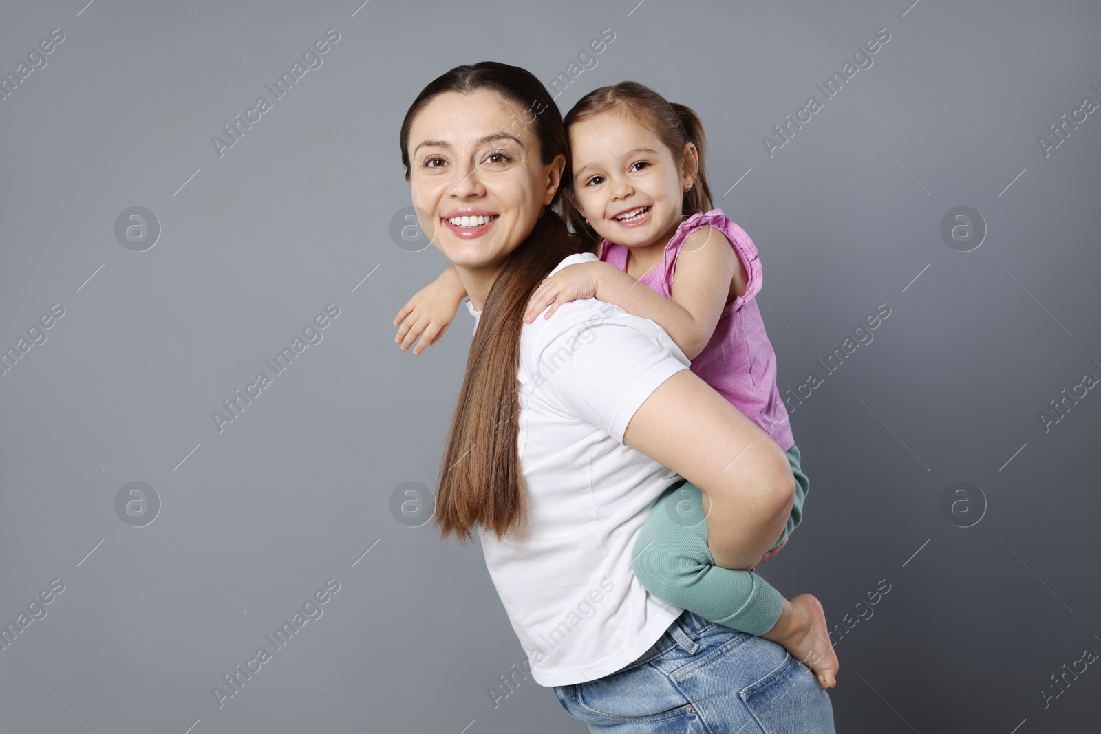 Photo of Portrait of happy mother and her cute little daughter on grey background, space for text