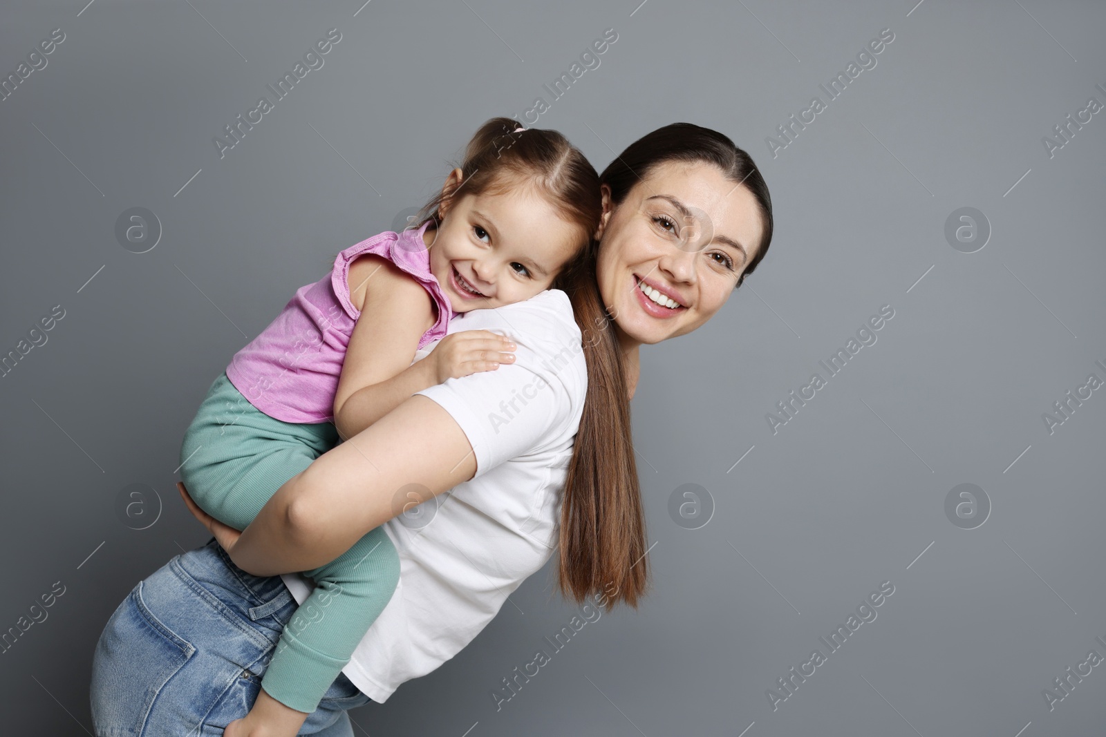 Photo of Portrait of happy mother and her cute little daughter on grey background, space for text