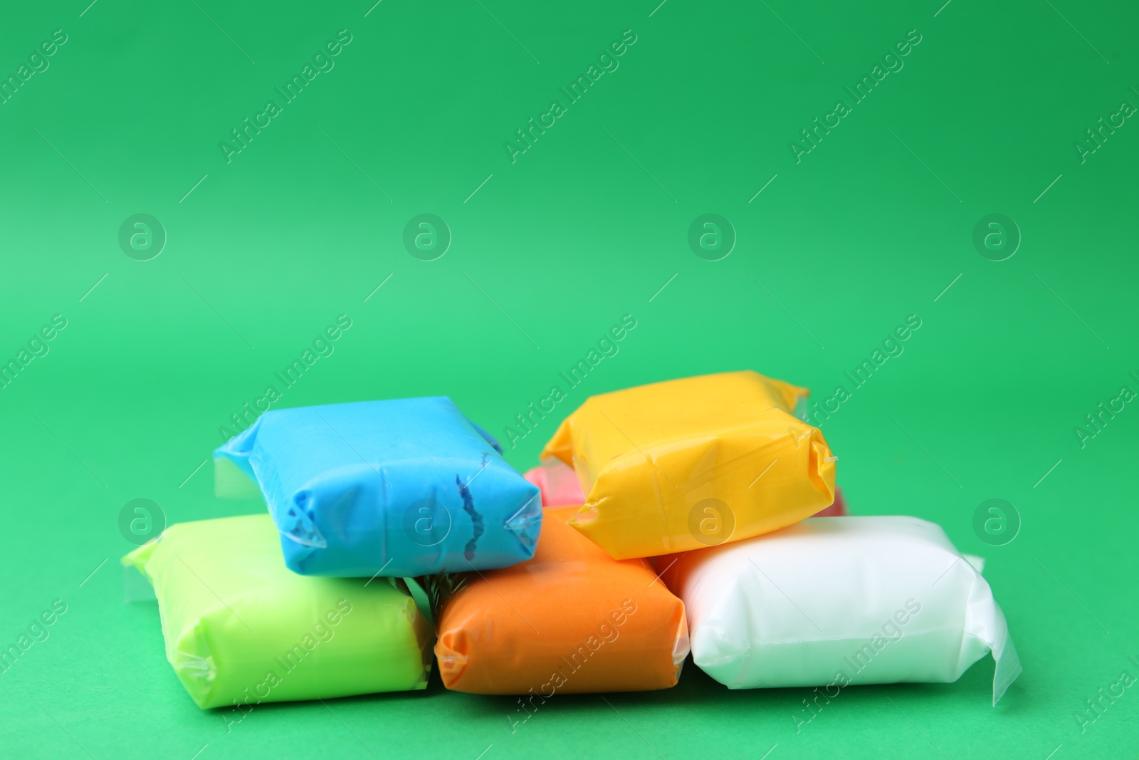 Photo of Different colorful play dough in packages on spring green background, closeup