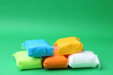 Photo of Different colorful play dough in packages on spring green background, closeup