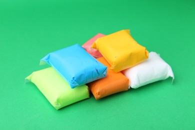 Photo of Different colorful play dough in packages on spring green background, closeup