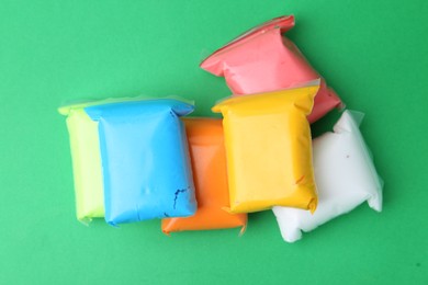 Photo of Different colorful play dough in packages on spring green background, top view