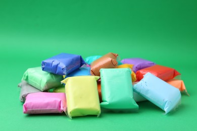 Photo of Different colorful play dough in packages on spring green background, closeup