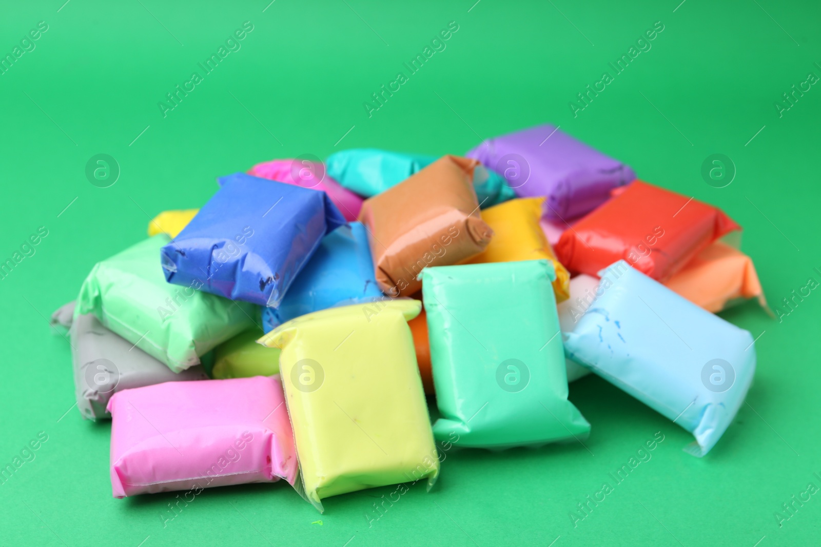 Photo of Different colorful play dough in packages on spring green background, closeup