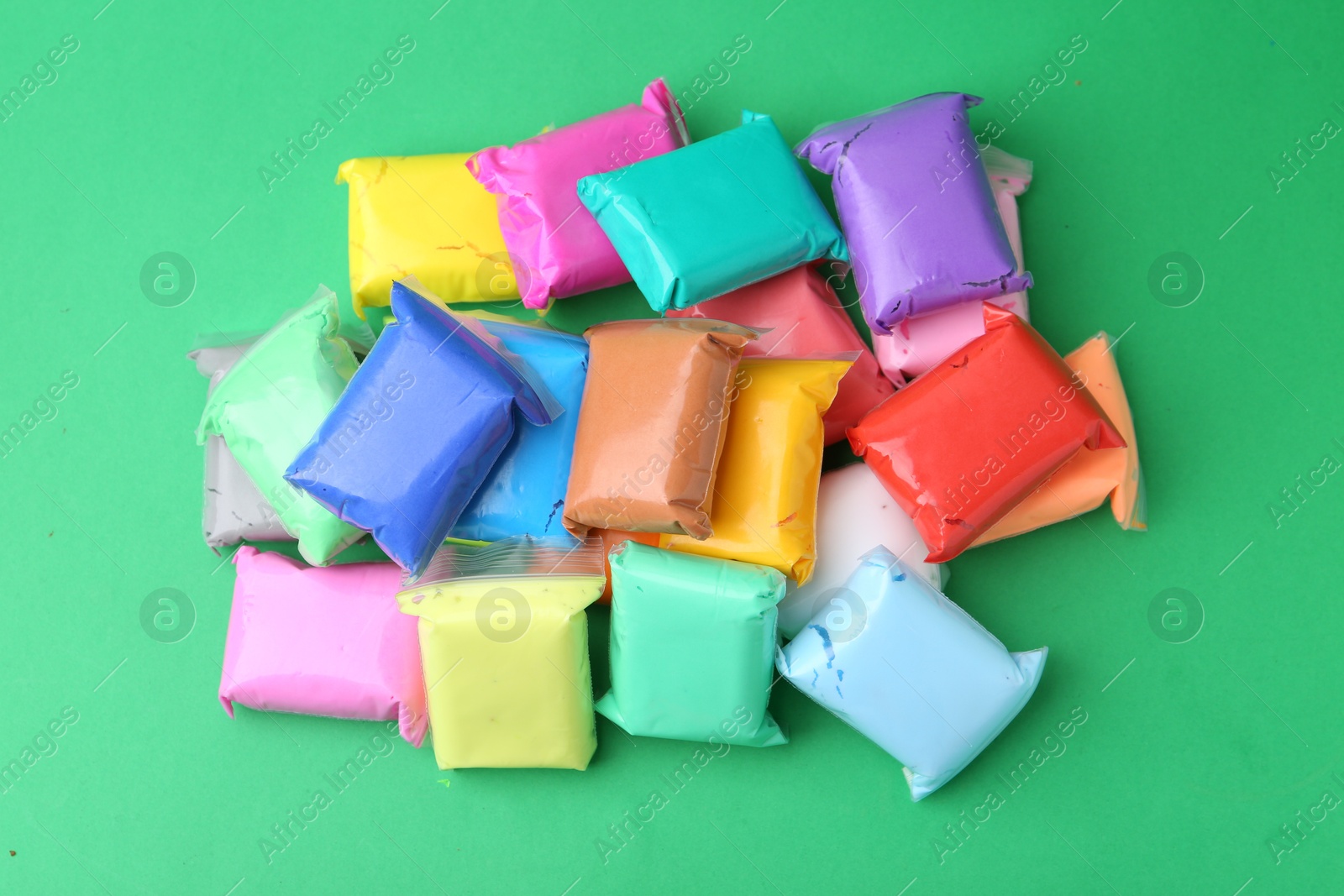 Photo of Different colorful play dough in packages on spring green background, top view