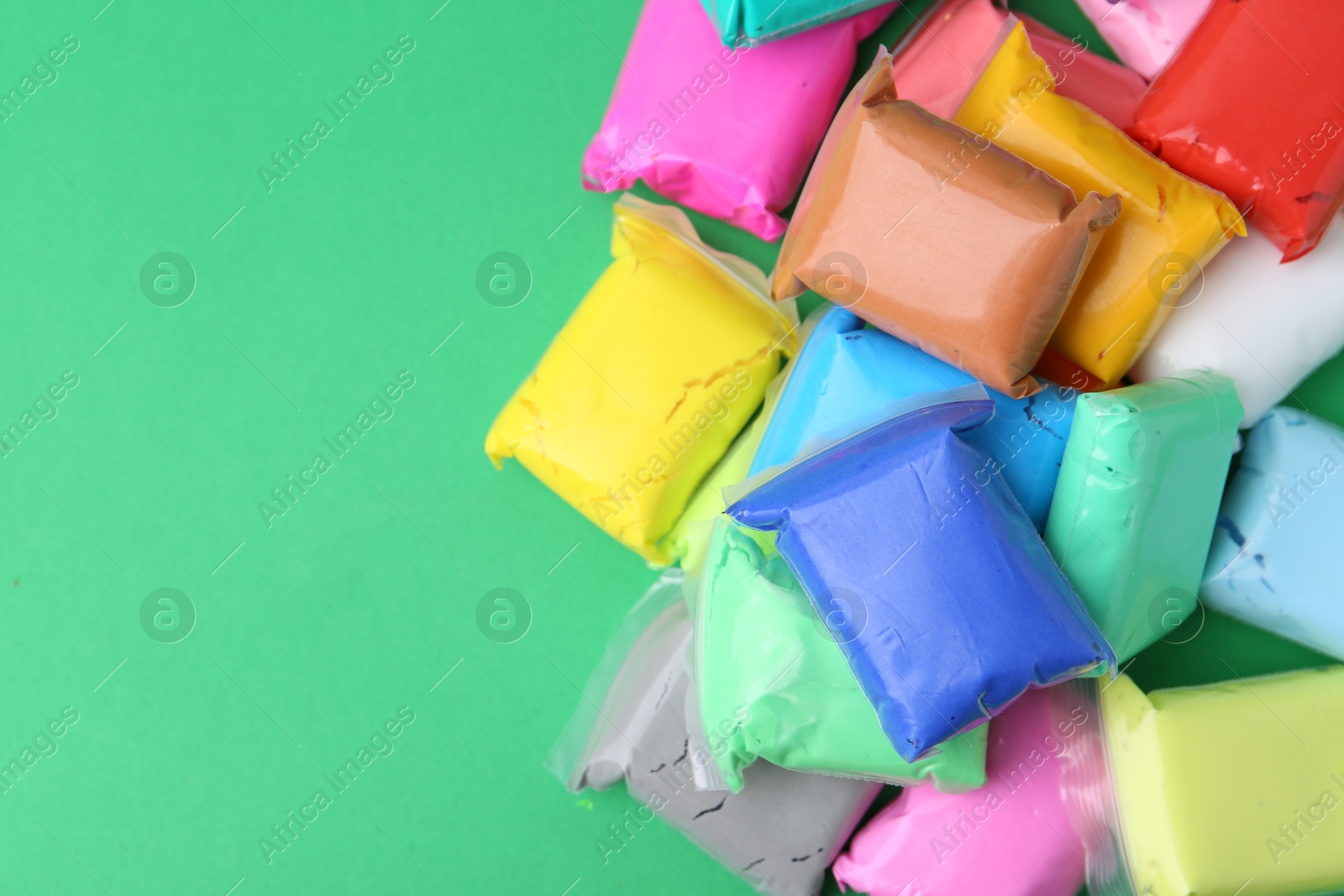 Photo of Different colorful play dough in packages on spring green background, top view. Space for text