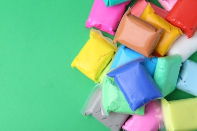 Photo of Different colorful play dough in packages on spring green background, top view. Space for text