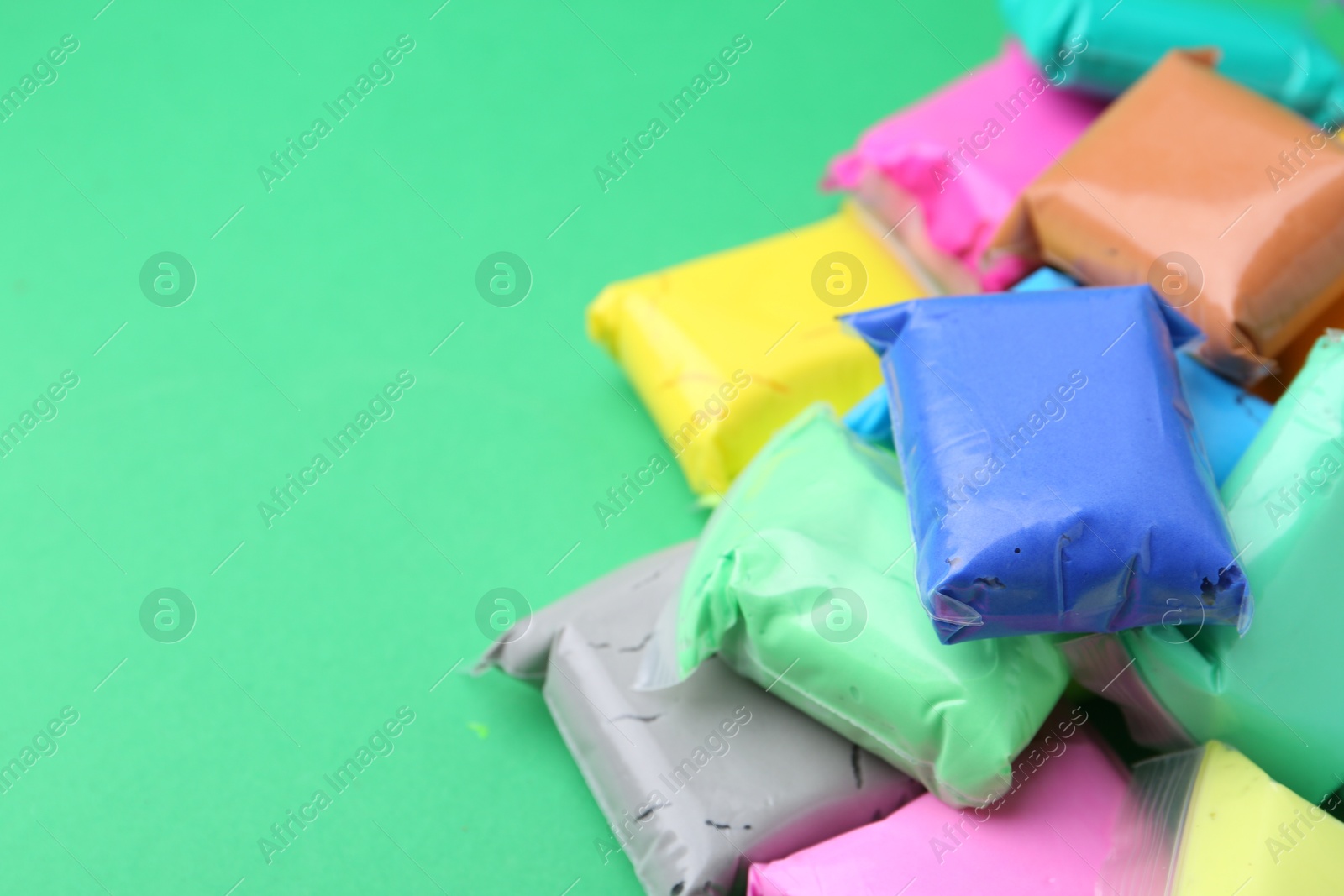 Photo of Different colorful play dough in packages on spring green background, closeup. Space for text