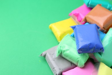 Photo of Different colorful play dough in packages on spring green background, closeup. Space for text