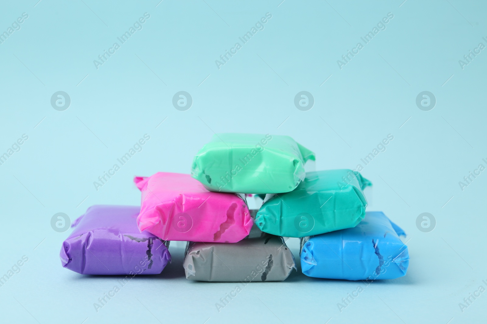 Photo of Different colorful play dough in packages on light blue background