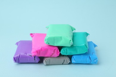 Photo of Different colorful play dough in packages on light blue background, closeup