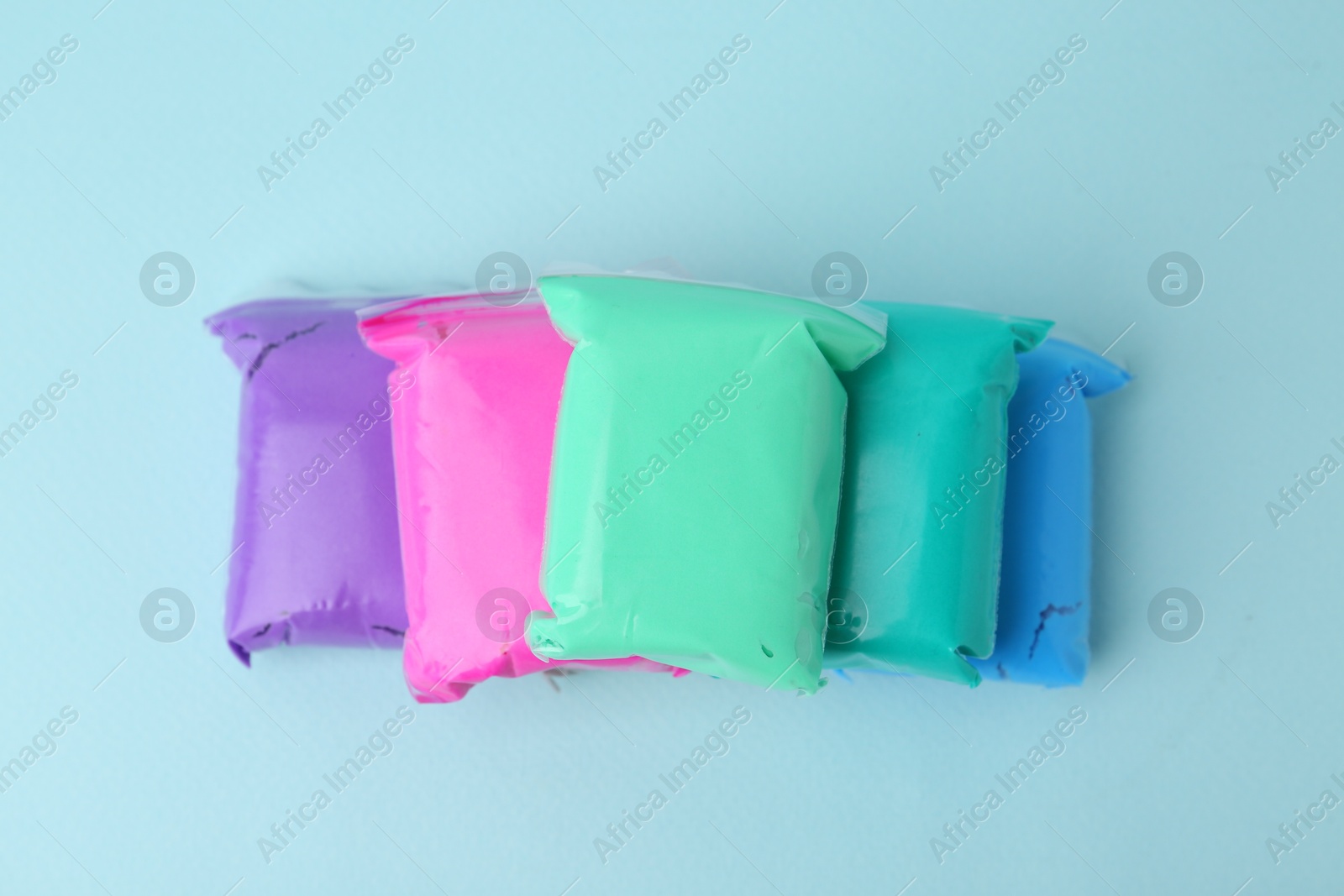 Photo of Different colorful play dough in packages on light blue background, top view