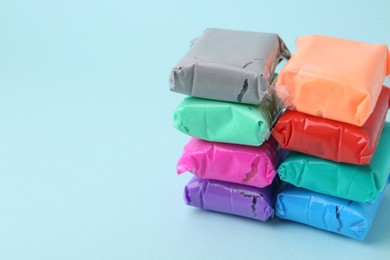 Photo of Different colorful play dough in packages on light blue background, closeup. Space for text