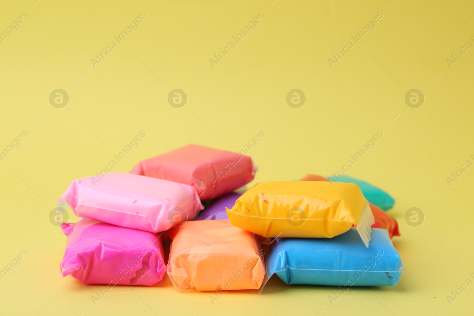 Photo of Different colorful play dough in packages on yellow background, closeup. Space for text